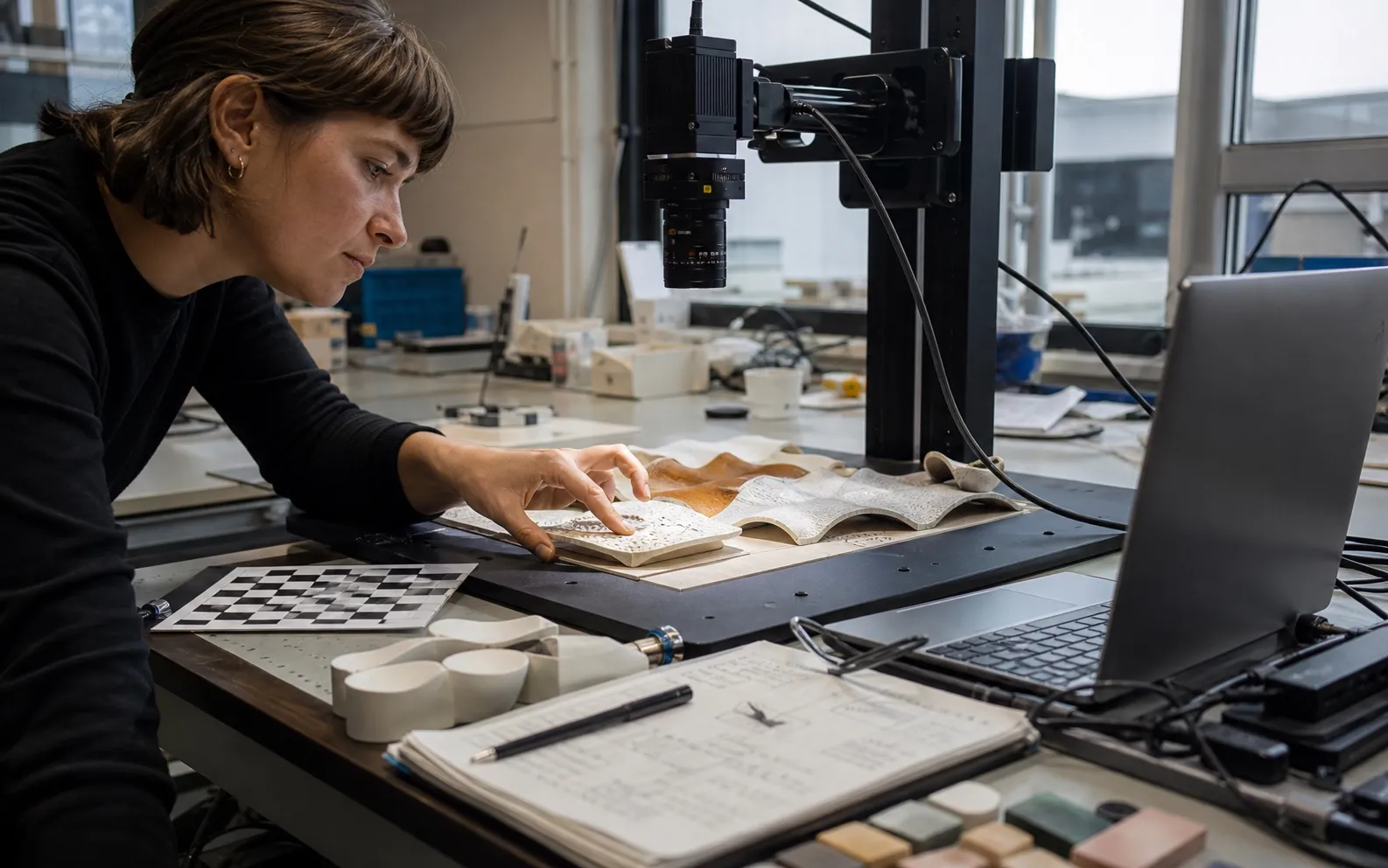 Researcher scanning a ceramic-and-textile prototype with an industrial camera in an applied AI materials lab